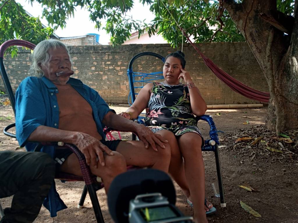 Malu sentada com seu avô cacique raoni em um quintal, em roda