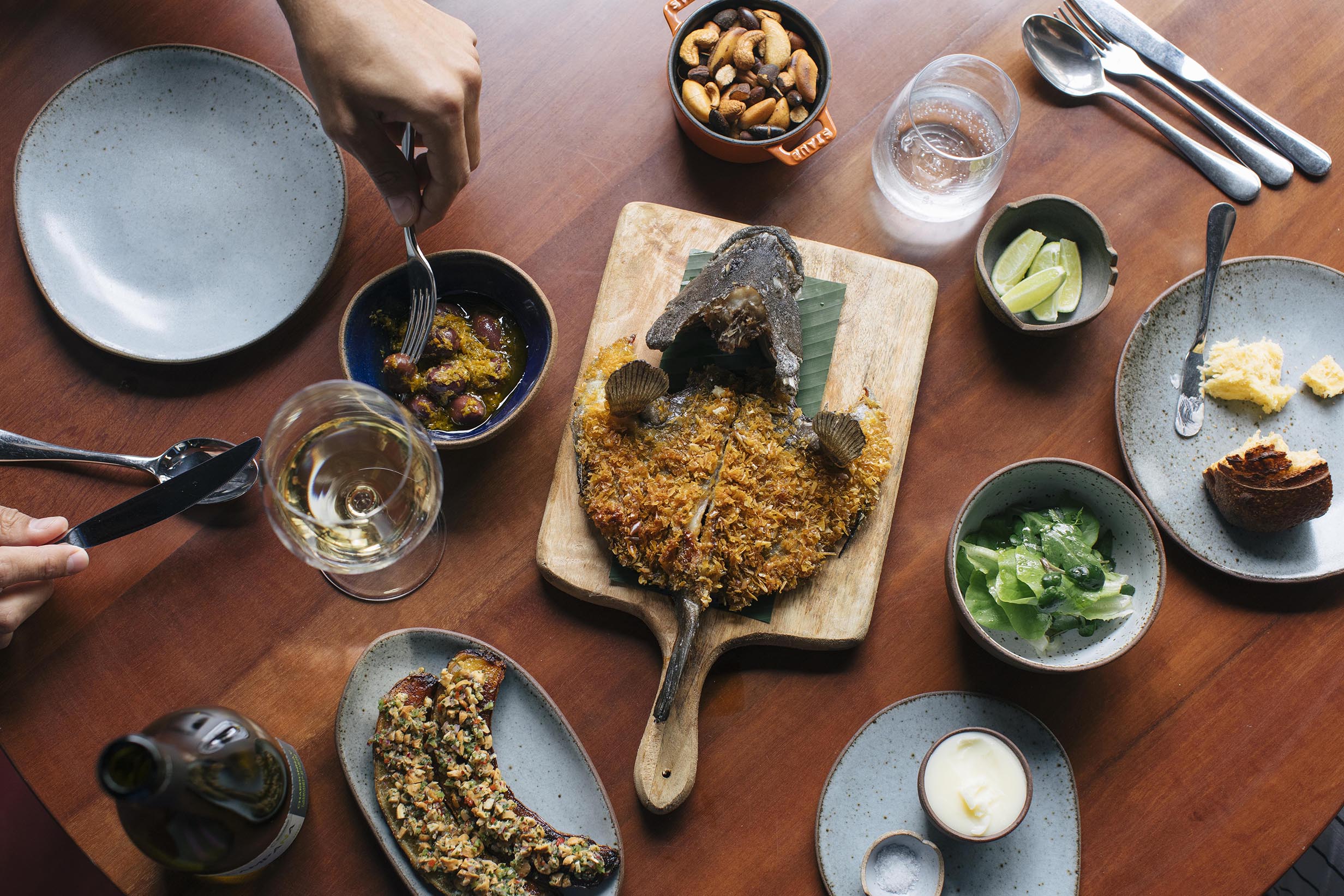 Fotografia de uma mesa vista de cima com um peixe e acompanhamentos ao redor