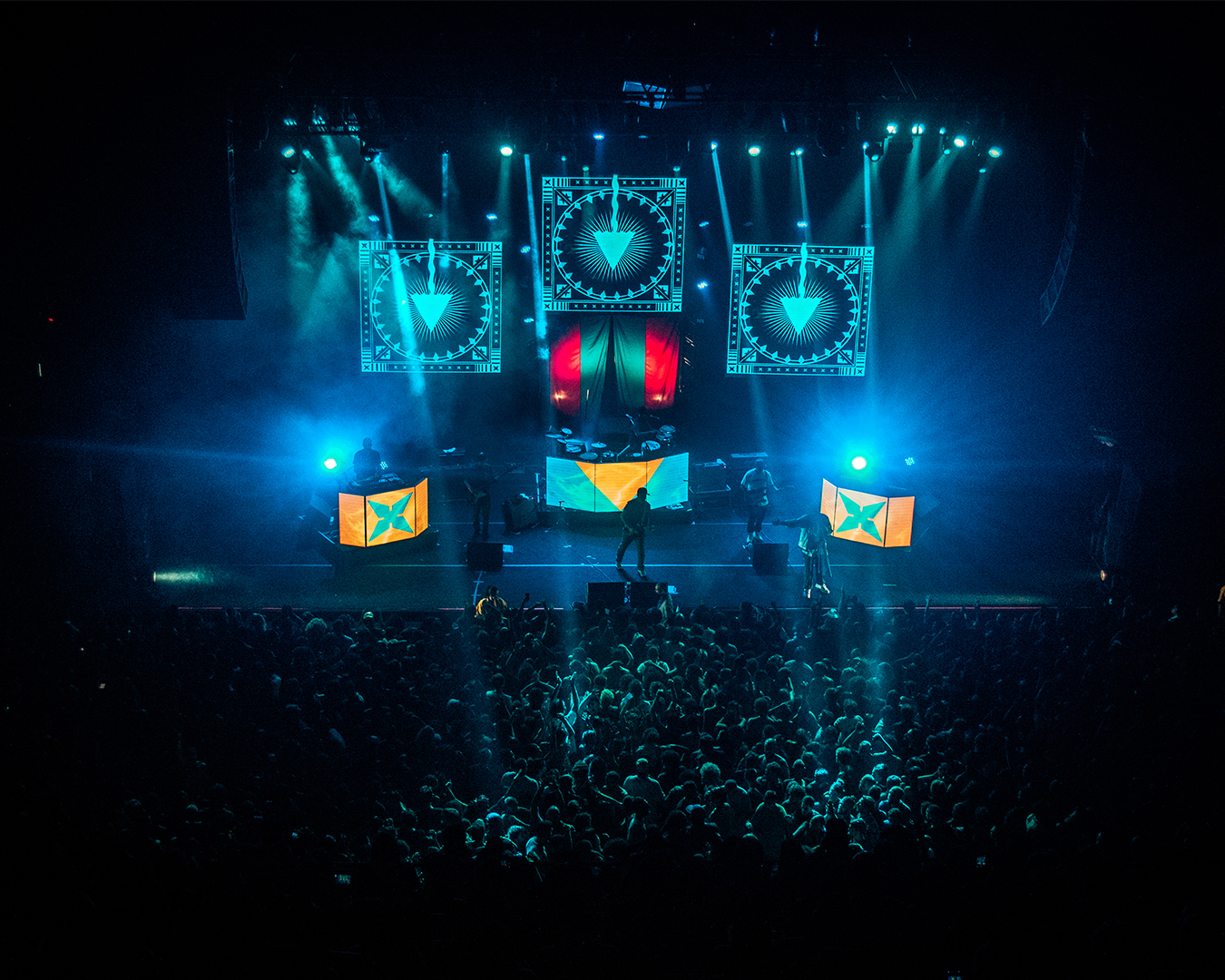 A banda Baiana System performando em palco com muitas luzes e telas, na frente deles é possível ver o público assistindo o show.