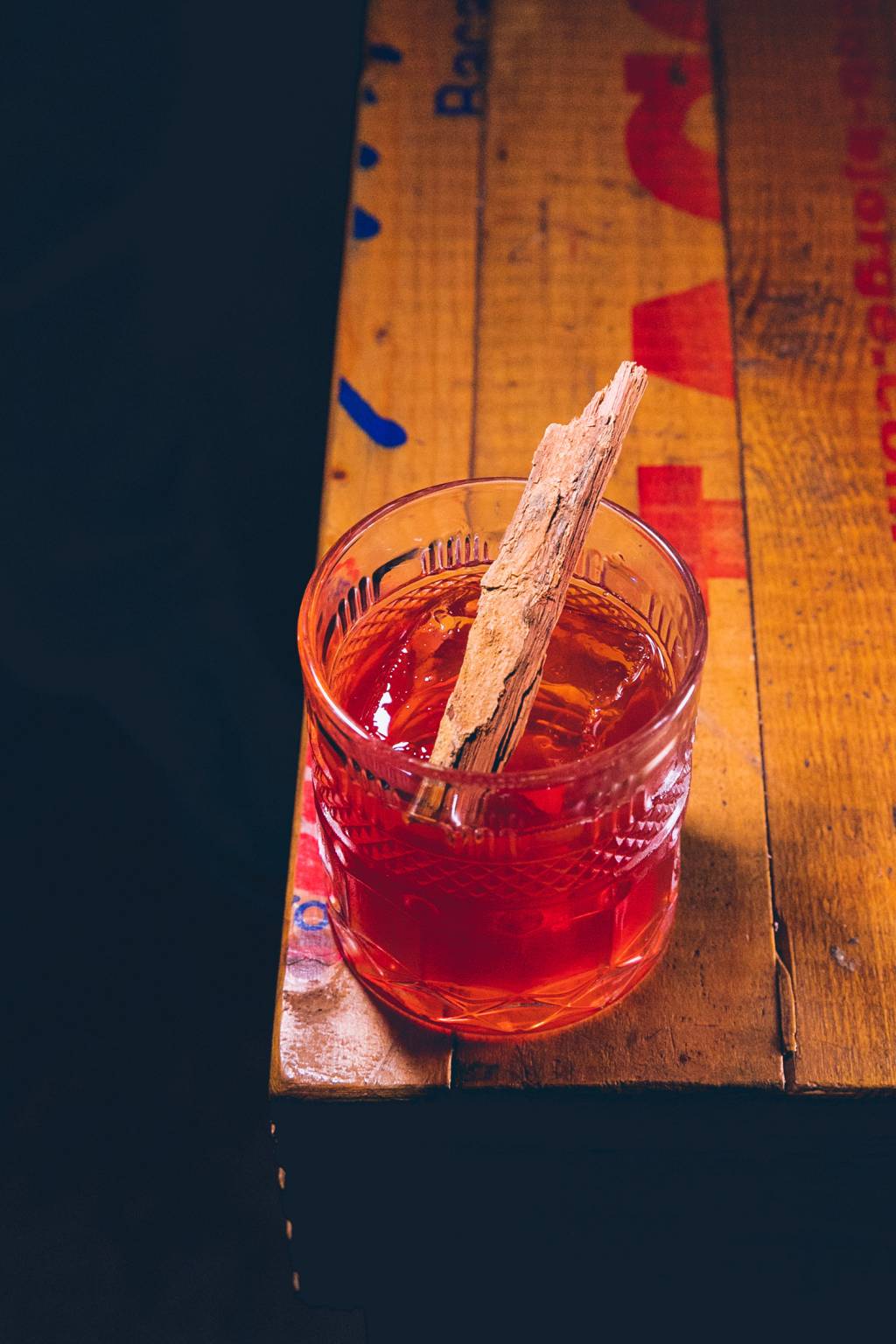 Drink de coloração avermelhada em cima de uma mesa de madeira.