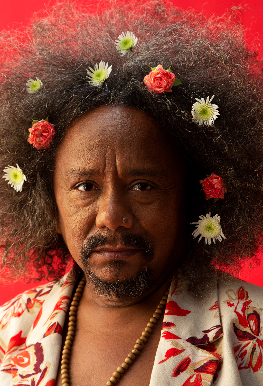 Fotografia do cantor e compositor Chico César. Ele veste um blazer florido e tem flores no cabelo.